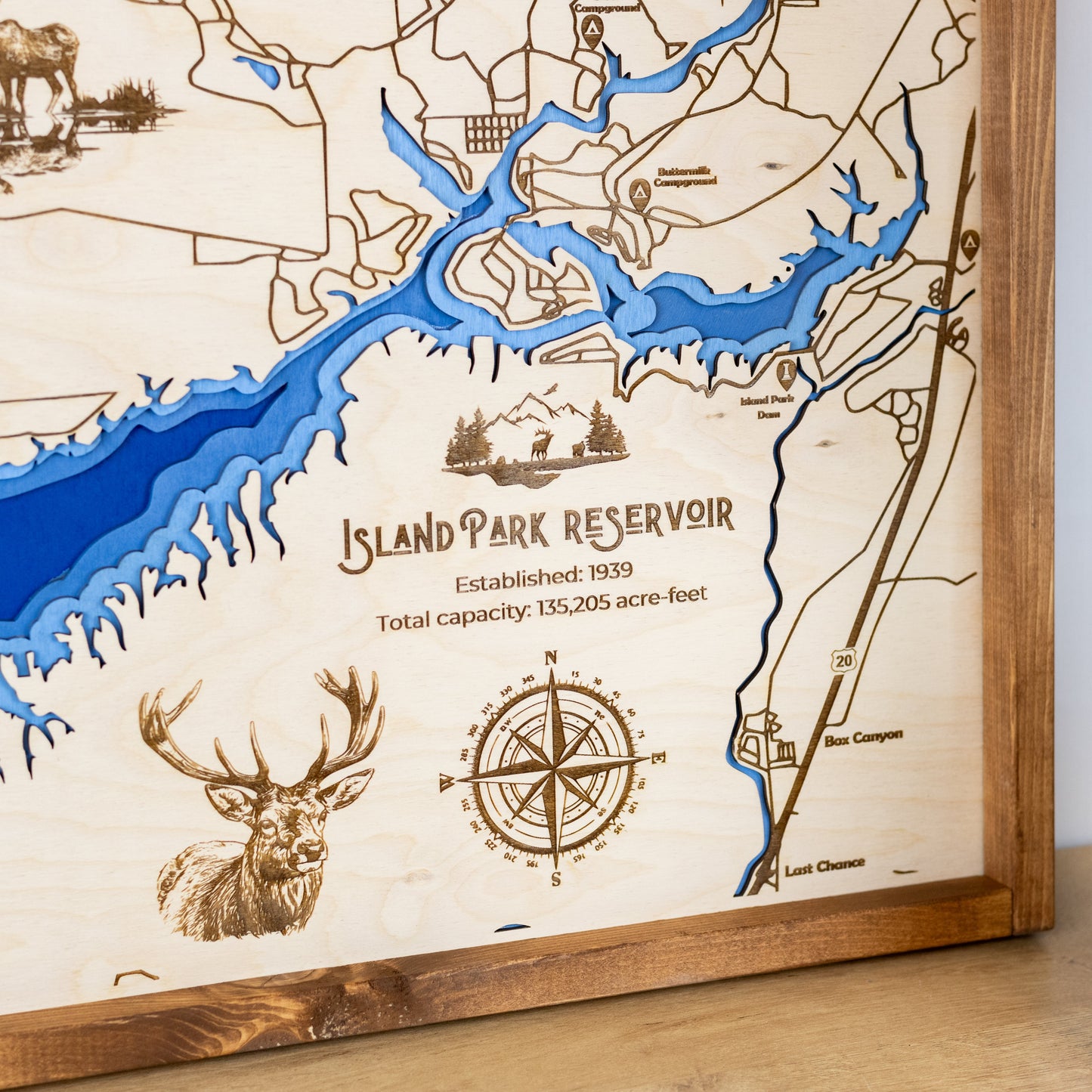 Close up of laser-engraved wood map of Island Park Reservoir featuring the lake, engraved wildlife, compass rose, trail and street names, and other landmarks.