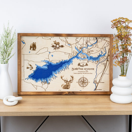 Laser-engraved wood map of Island Park Reservoir featuring lakes, rivers, and engraved wildlife, with labeled trails and landmarks.