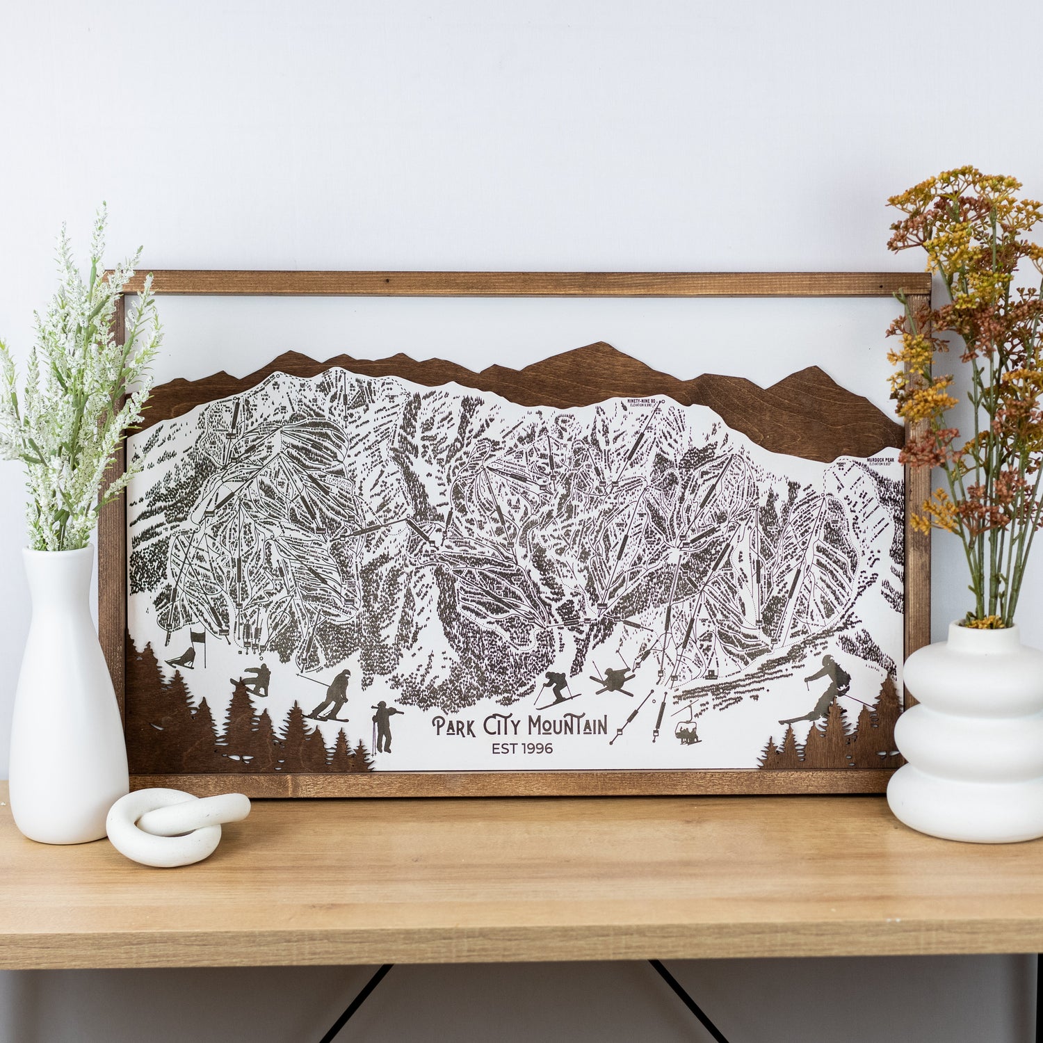 Laser-engraved wooden trail map of Park City Mountain with skier silhouettes and mountain outline, resting on a shelf