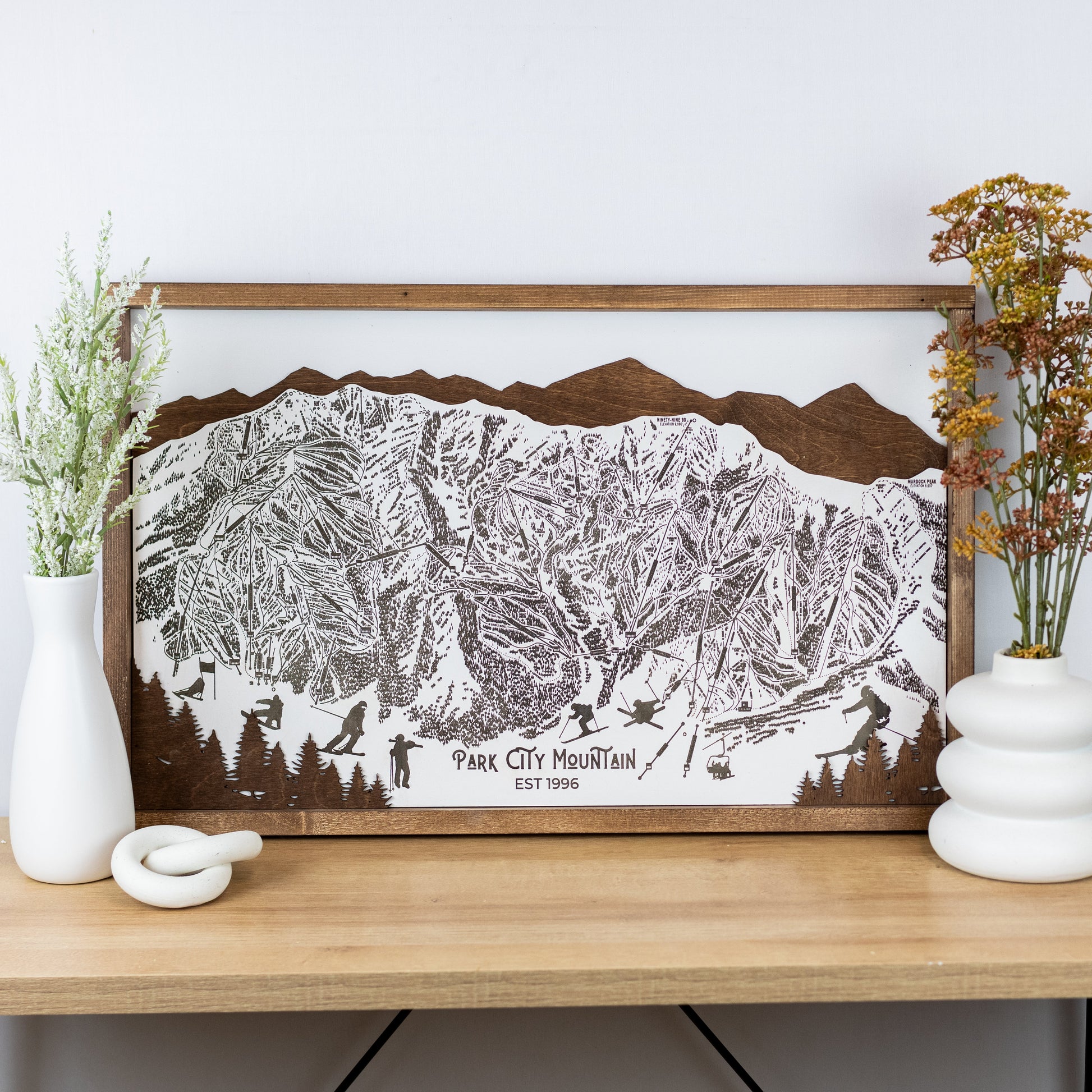 Laser-engraved wooden trail map of Park City Mountain with skier silhouettes and mountain outline, resting on a shelf