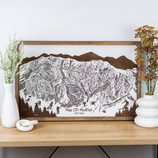 Laser-engraved wooden trail map of Park City Mountain with skier silhouettes and mountain outline, resting on a shelf